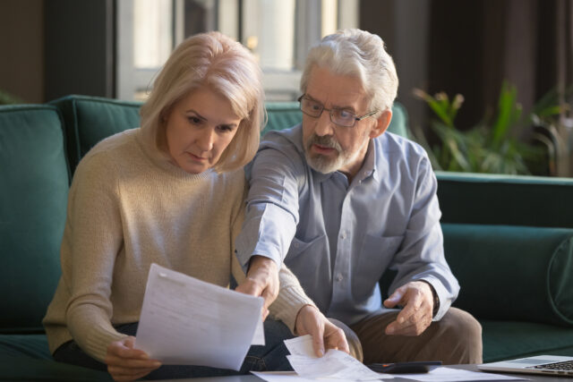 Serious grey haired mature couple calculating bills, checking finances together