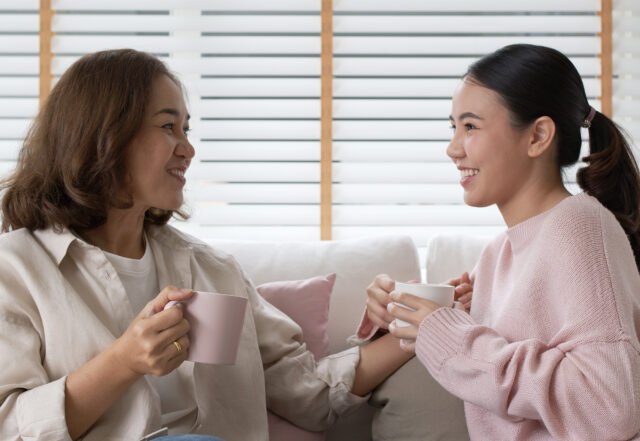 Adult daughter with mom sitting on a couch drinking coffee