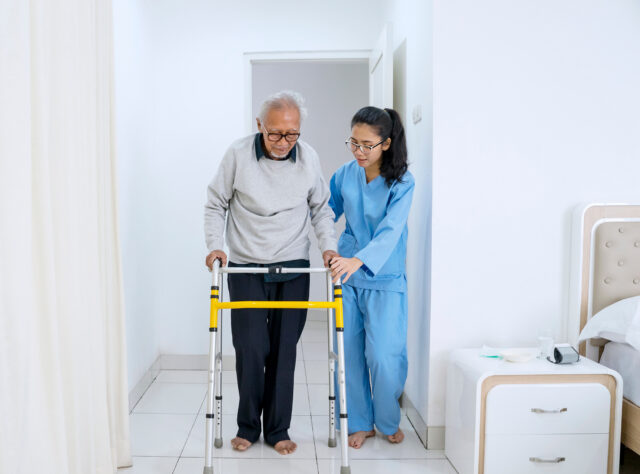 Older man using walker with the help of a young nurse