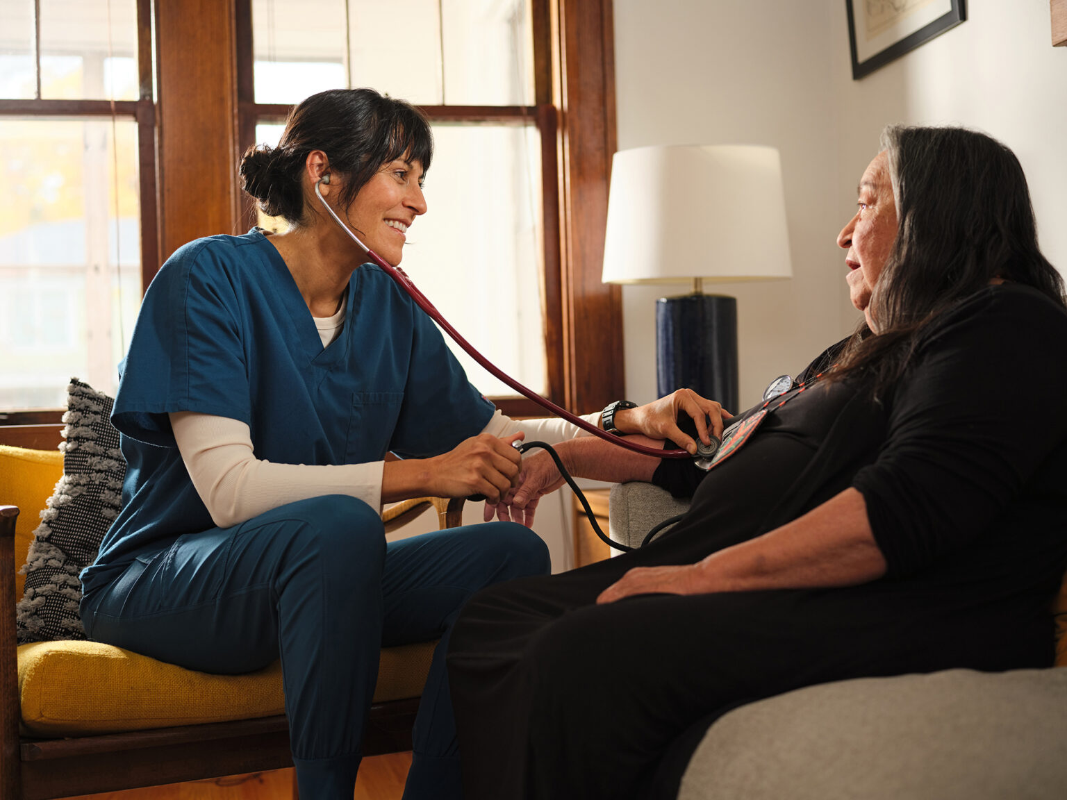 nurse listens to blood pressure of senior woman at home